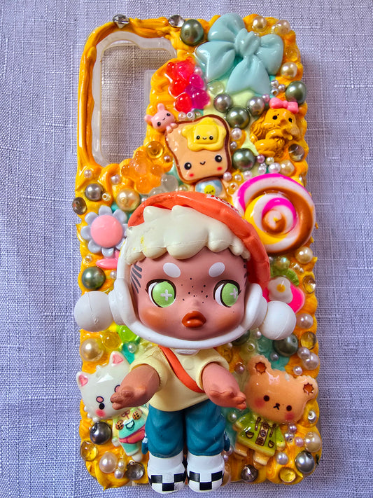 Handmade Samsung S23 Plus phone case with colorful kawaii and toy-themed 3D decorations, featuring a doll figure, pearls, cartoon charms, and candy accents on a yellow base.
