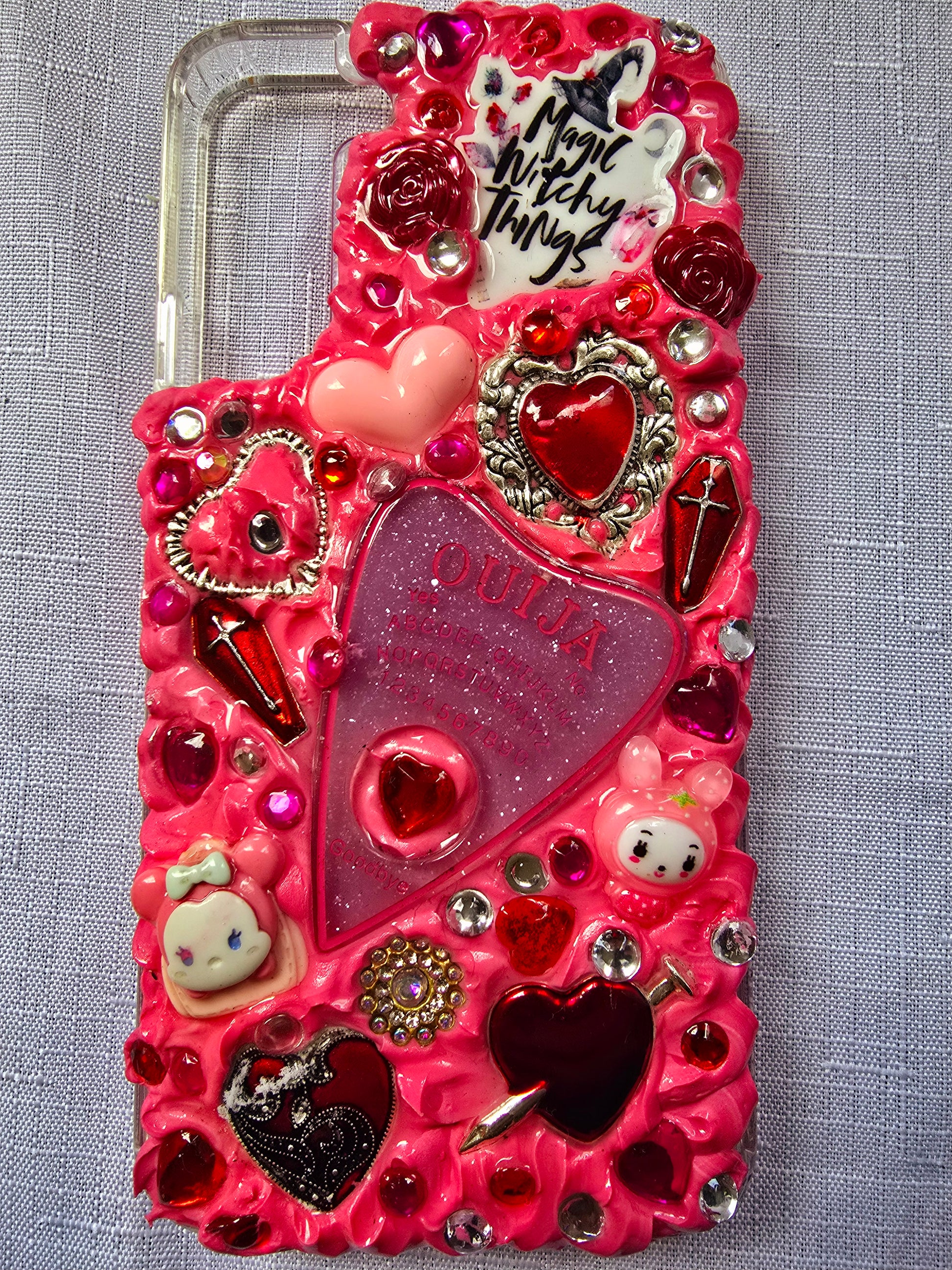 Handmade Samsung S22 Plus phone case with a pink, red, and black witchy kawaii theme, featuring a Ouija planchette, heart charms, My Melody figures, and cute gothic embellishments.