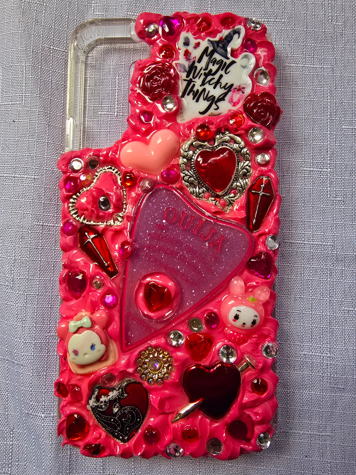 Handmade Samsung S22 Plus phone case with a pink, red, and black witchy kawaii theme, featuring a Ouija planchette, heart charms, My Melody figures, and cute gothic embellishments.