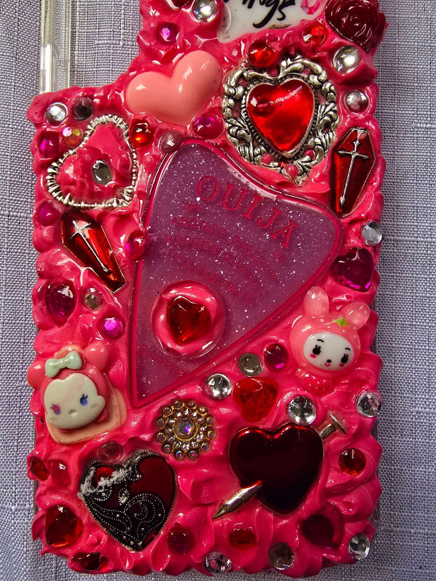 Handmade Samsung S22 Plus phone case with a pink, red, and black witchy kawaii theme, featuring a Ouija planchette, heart charms, My Melody figures, and cute gothic embellishments.
