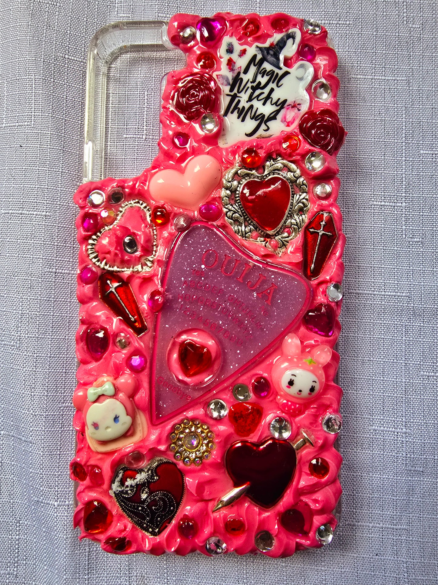 Handmade Samsung S22 Plus phone case with a pink, red, and black witchy kawaii theme, featuring a Ouija planchette, heart charms, My Melody figures, and cute gothic embellishments.