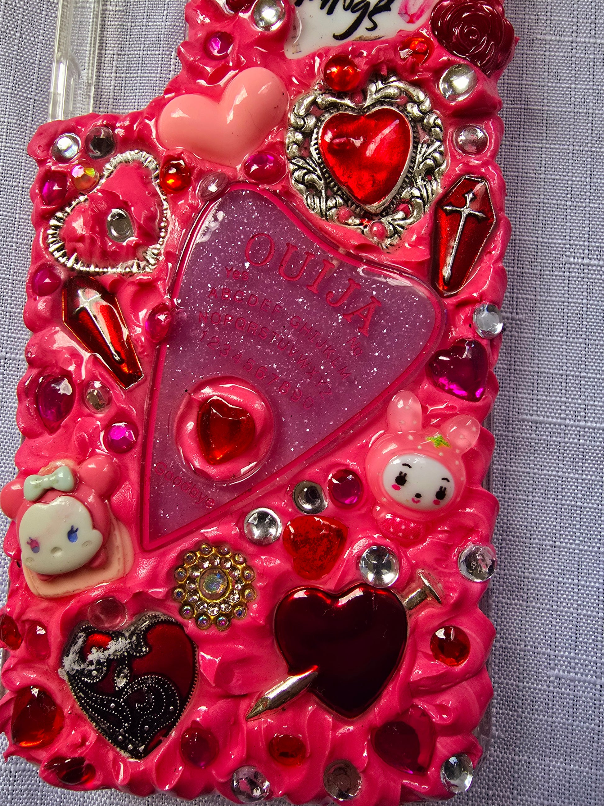 Handmade Samsung S22 Plus phone case with a pink, red, and black witchy kawaii theme, featuring a Ouija planchette, heart charms, My Melody figures, and cute gothic embellishments.