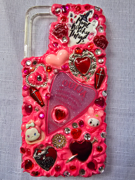Handmade Samsung S22 Plus phone case with a pink, red, and black witchy kawaii theme, featuring a Ouija planchette, heart charms, My Melody figures, and cute gothic embellishments.